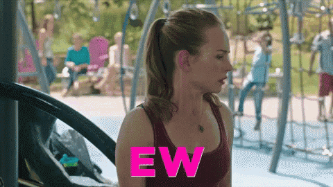 a woman in a red tank top is standing in front of a playground with the word ew written in pink