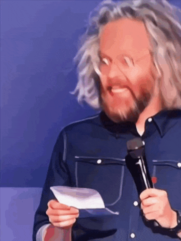 a man with long hair and a beard is holding a microphone and a piece of paper .