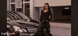 a woman in a black suit is standing next to a black mercedes benz .