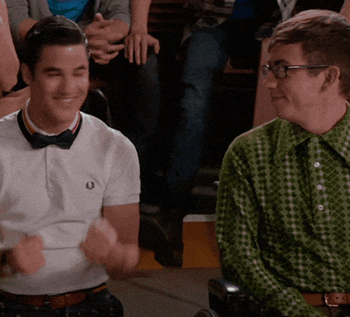 a man wearing a bow tie is sitting next to another man wearing a green shirt