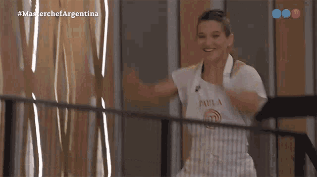 a woman in an apron is standing on a balcony with her arms outstretched and smiling .