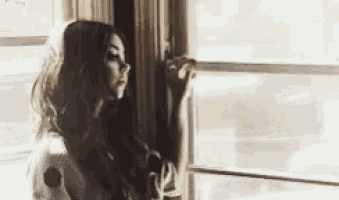a woman is standing in front of a window looking out of it .