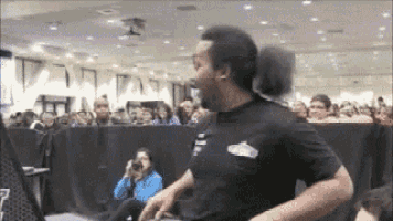 a man in a black shirt is standing in front of a crowd in a room .
