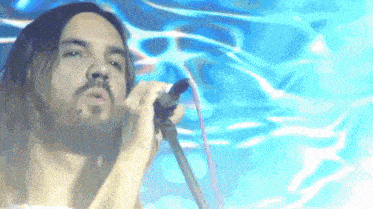a man with long hair singing into a microphone with a blue background