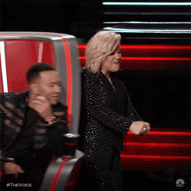 a woman in a black suit is standing next to a man in a black suit on nbc 's the voice show