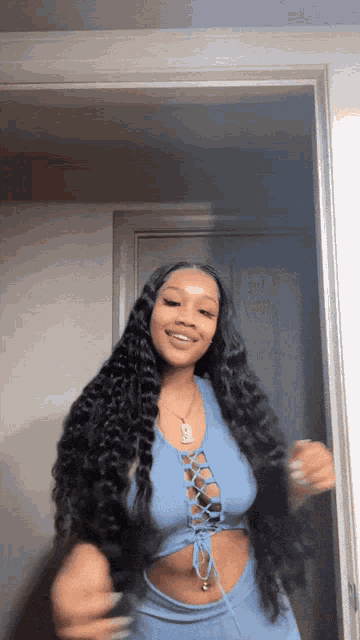 a woman with long hair is standing in a doorway wearing a blue crop top .