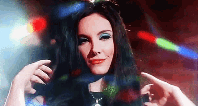 a woman with long black hair and blue eye makeup is standing in front of a disco light .