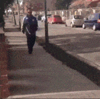 a man walking down a sidewalk with cars parked on the side of the road
