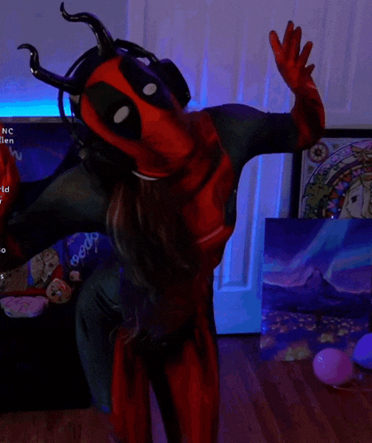 a woman in a deadpool costume stands in front of a tv screen that says nc garden world