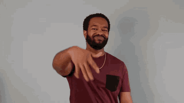 a man with a beard wearing a maroon t-shirt is waving his hand