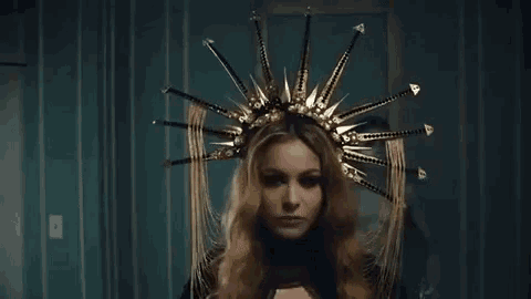 a woman wearing a crown of spikes on her head is standing in a dark room .
