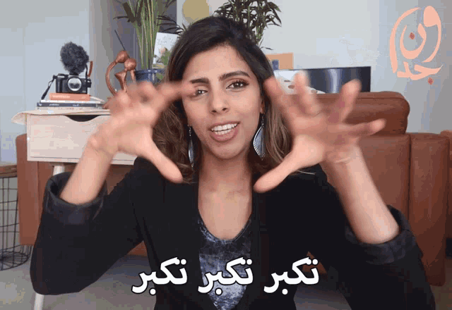 a woman in a black jacket is making a hand gesture with arabic writing behind her