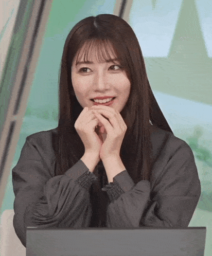 a woman in a grey shirt is smiling with her hands on her chin