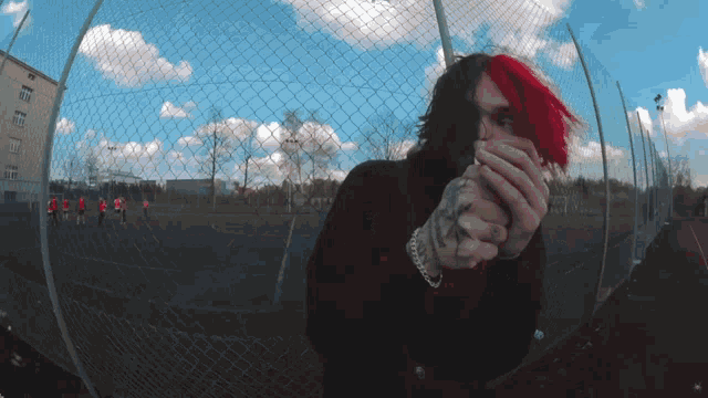 a man with red hair is standing in front of a fence