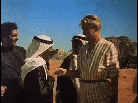 a group of men are standing in the desert talking to each other and shaking hands .