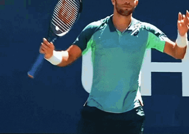 a man in a blue shirt is holding a tennis racquet in front of a blue wall with the letter h on it