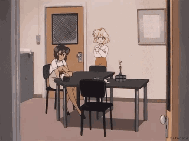 two women are sitting at a table in a room with a door in the background .