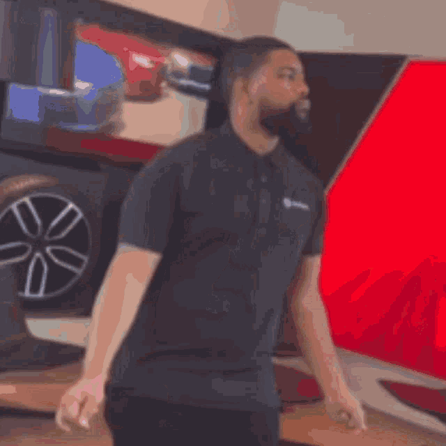 a man in a black shirt is standing in front of a red wall with a picture of a car on it .