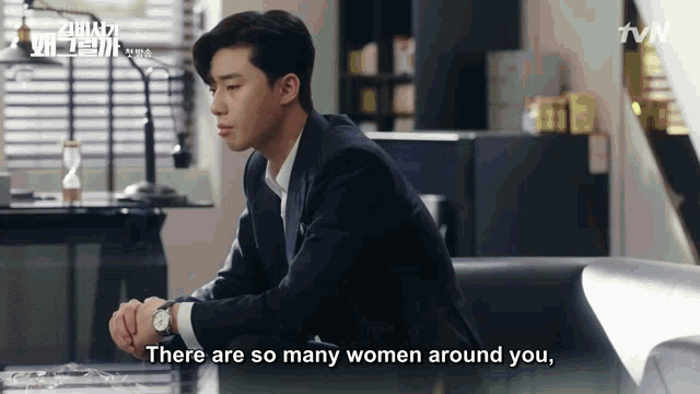 a man in a suit is sitting on a couch and says " there are so many women around you "