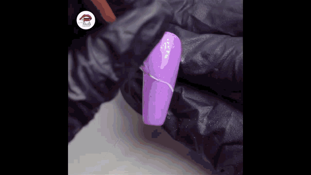 a person wearing black gloves is applying purple nail polish to a purple nail .
