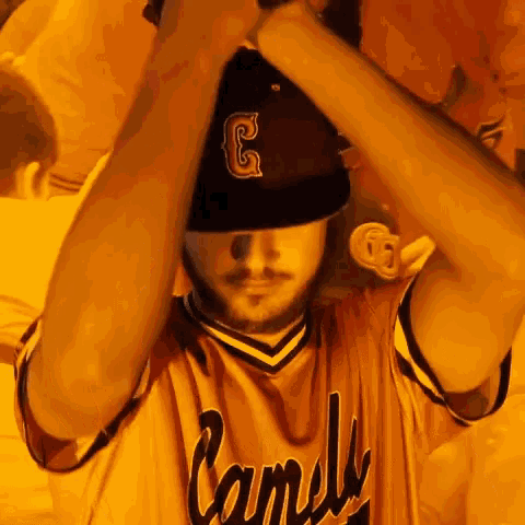 a man wearing a camels jersey adjusts his baseball cap