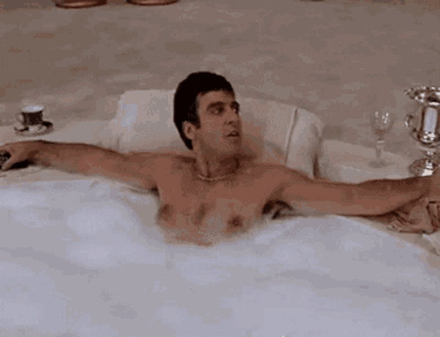 a shirtless man is taking a bath in a bathtub with his arms outstretched .