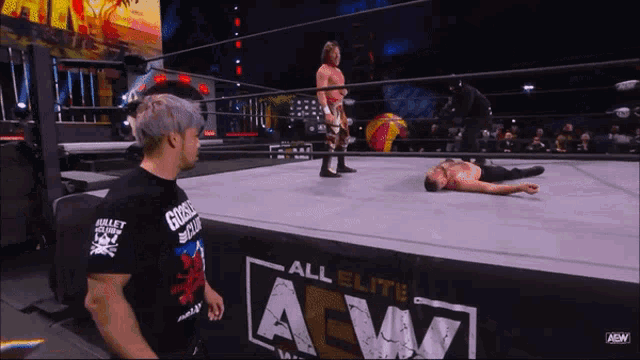 a wrestler is laying on the ground in front of a banner that says all elite aew on it