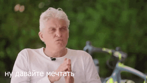 a man in a white shirt is speaking in a foreign language with a bicycle in the background