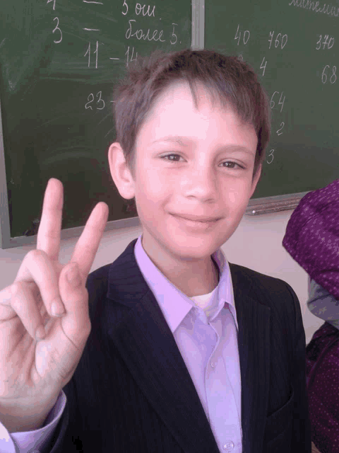 a boy giving a peace sign in front of a blackboard