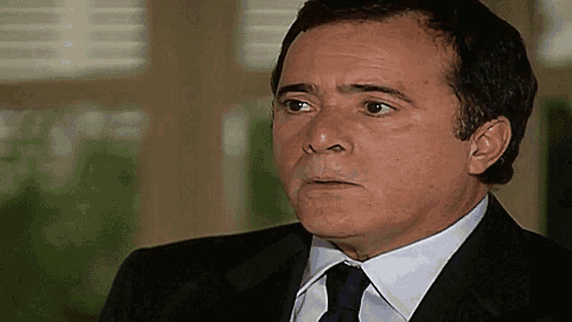 a man in a suit and tie looks at the camera with a serious look on his face