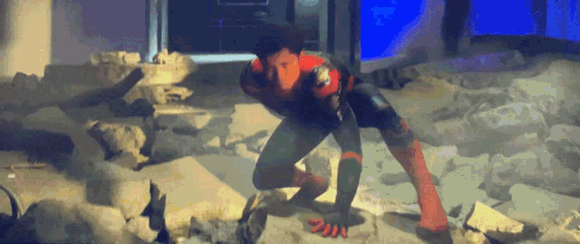 a man in a spiderman suit is crawling on a rocky floor