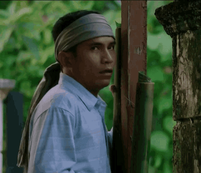 a man wearing a headband and a blue shirt is leaning against a wooden post