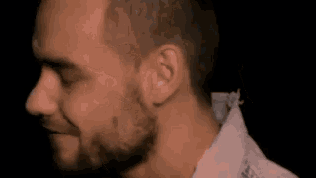 a man with a beard is wearing a white shirt and looking down .
