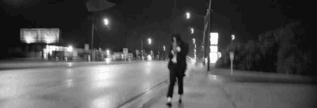 a black and white photo of a person walking down a sidewalk at night .