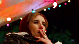 a woman is smoking a cigarette in front of a string of christmas lights