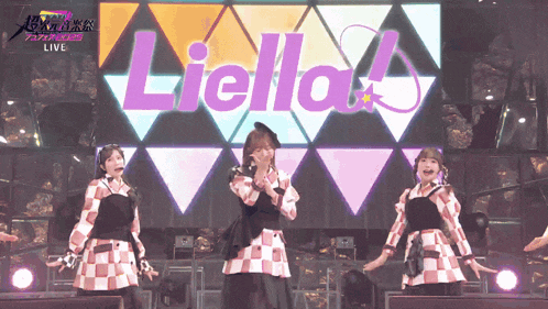 three women singing on a stage with the word liella behind them