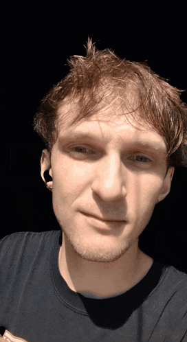 a man wearing a black shirt and earbuds looks at the camera
