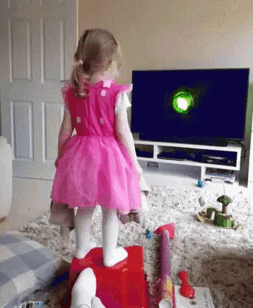 a little girl in a pink dress is standing in front of a tv