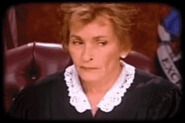 a female judge is sitting in a courtroom wearing a black robe and white collar .