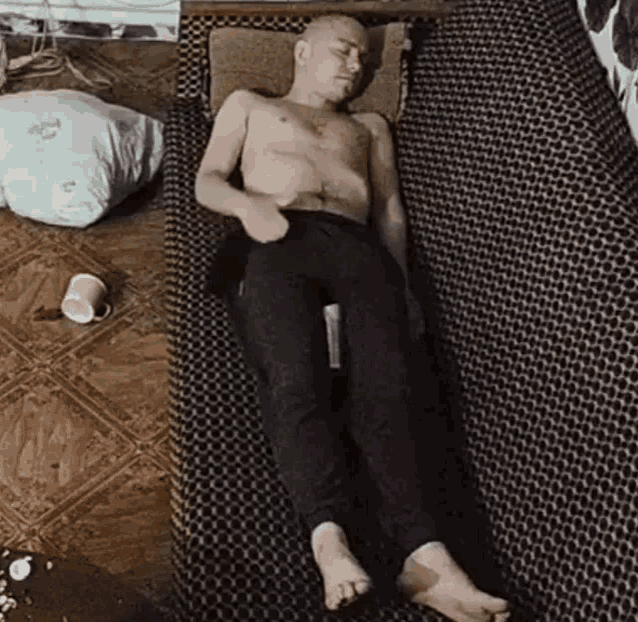 a shirtless man is laying on a bed with a bottle of alcohol in his hand .
