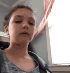 a young girl is standing in front of a window making a funny face .