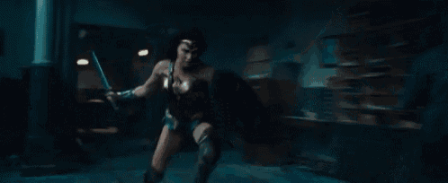 wonder woman is holding a sword in her hand in a dark room .