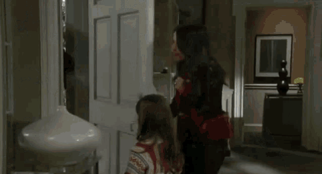 a man and two women are standing in a living room . the woman is wearing a red shirt .