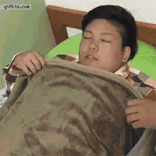 a man is laying in bed with his eyes closed and holding a blanket over his head .