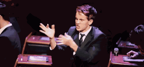 a man in a suit and tie is standing in front of a microphone with his arms outstretched .