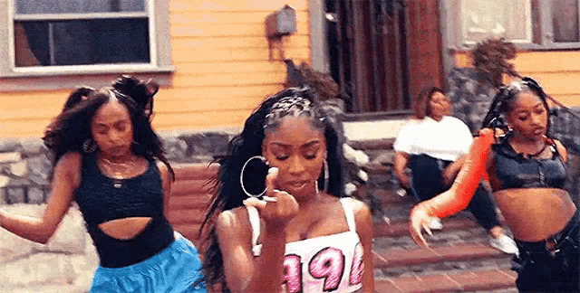 a group of women are dancing in front of a house .
