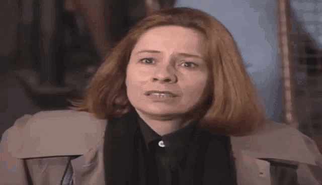 a woman with red hair is wearing a trench coat and a black shirt and is making a funny face .