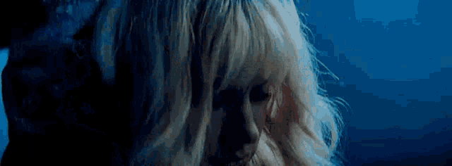 a close up of a woman 's face with blonde hair in the dark .