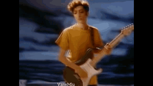 a man in a yellow shirt is playing a guitar in a video .