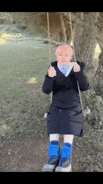 a person with pink hair is sitting on a swing in the woods